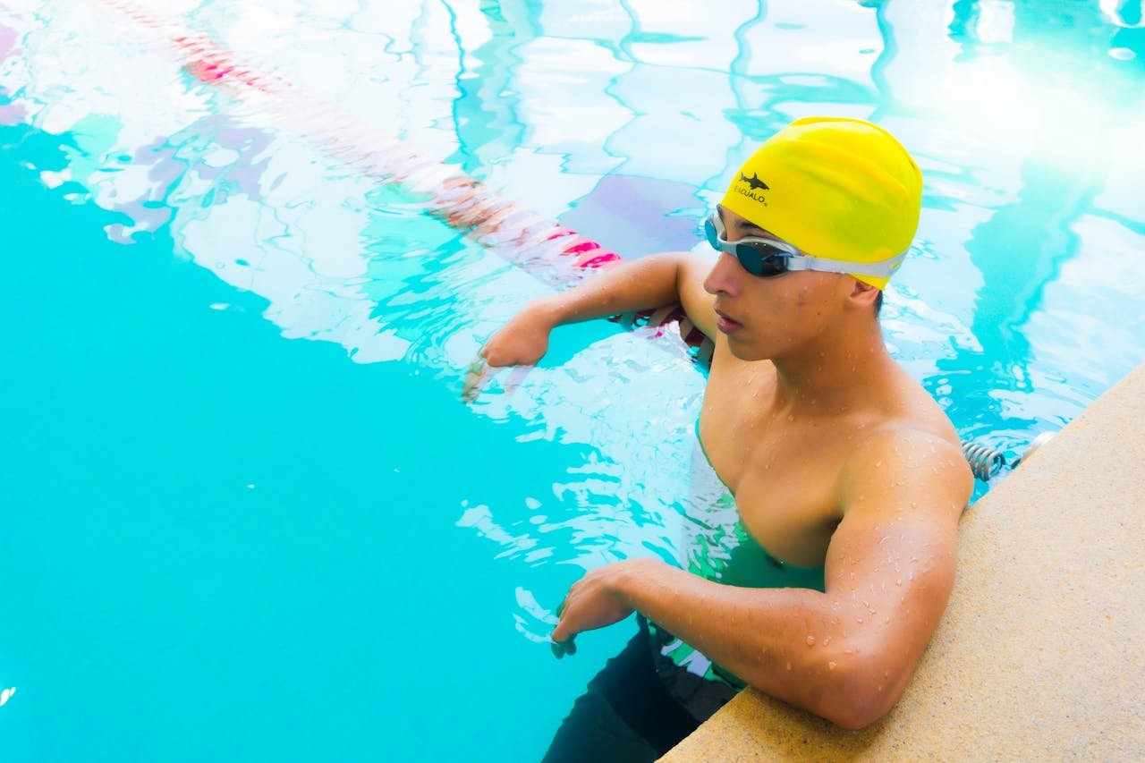 Adult male swimmer with yellow swim cap training in outdoor pool.